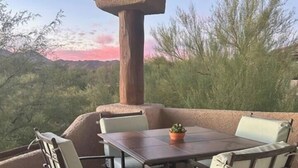 An outdoor patio with a table and chairs, a potted plant, and a view of trees and a sunset. - Welcome to Resort Casita (Oro Valley)