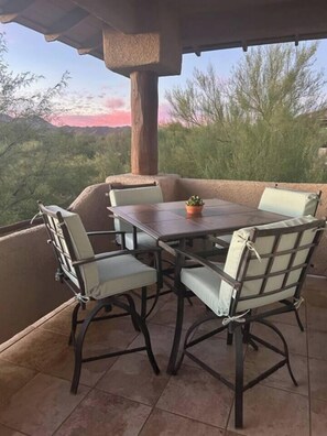 Patio esterno con tavolo e sedie, una pianta in vaso e vista su alberi e tramonto.