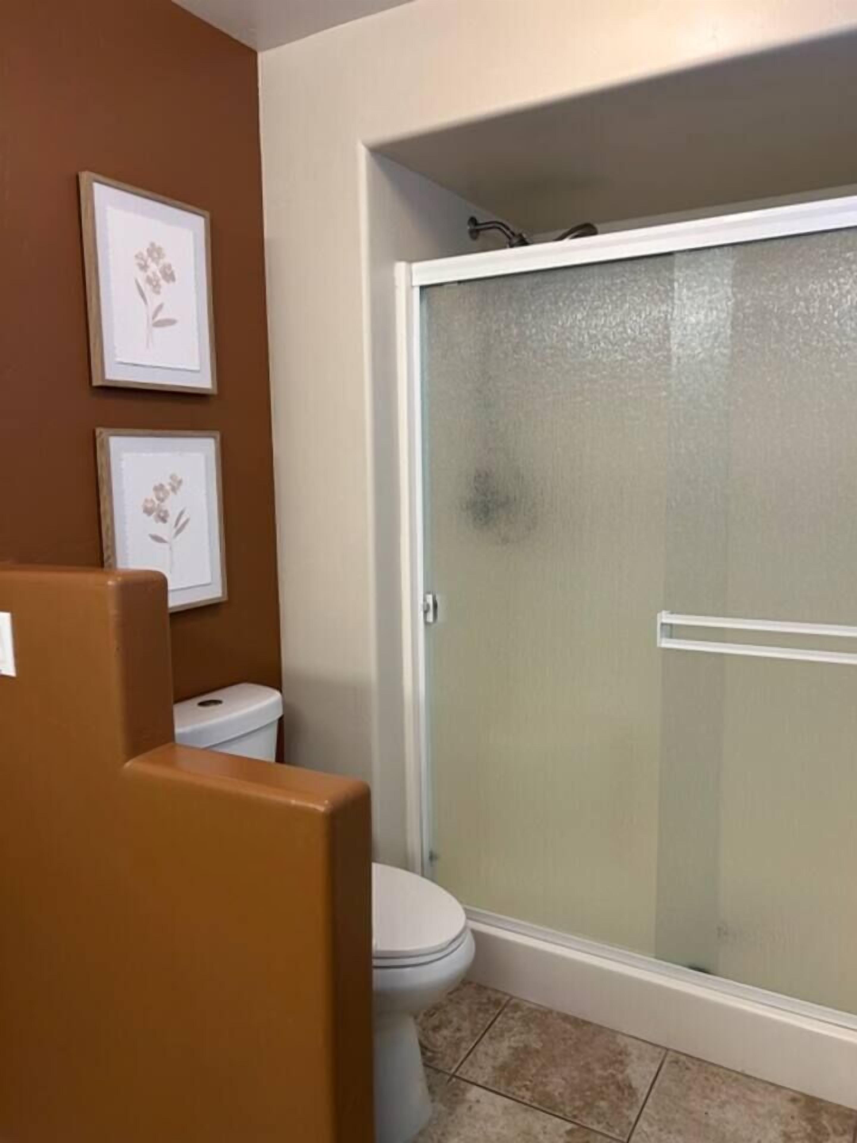 A bathroom with a toilet, a shower with a glass door, and two framed pictures on the wall.