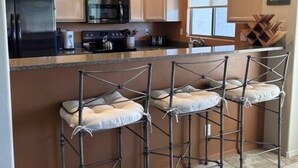 A kitchen with white cabinets, a black refrigerator, a microwave, and a stove. There are three metal bar stools with cushions. - Welcome to Resort Casita (Oro Valley)