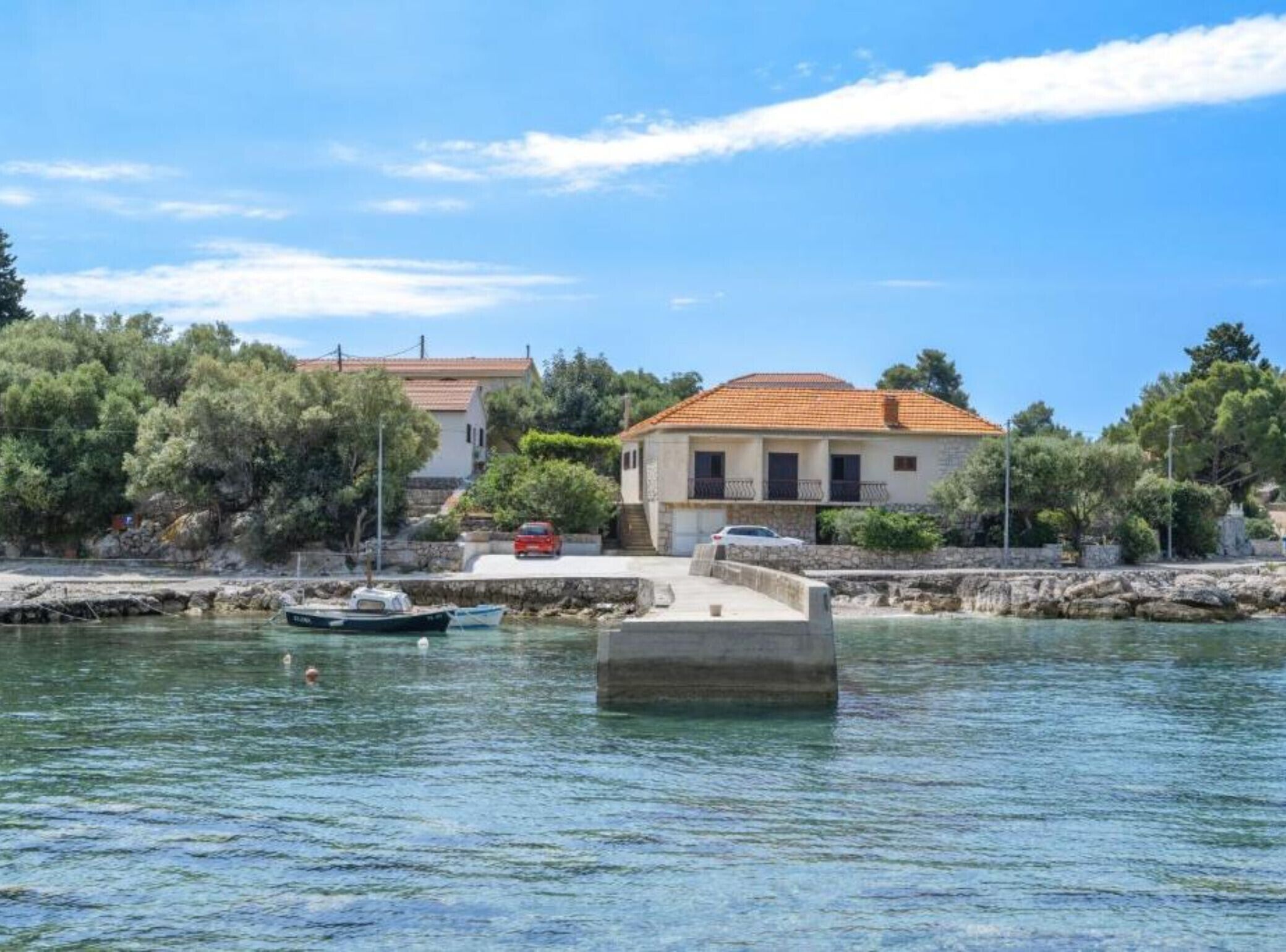 Une propriété située sur la côte, avec une jetée en pierre qui s’avance dans l’eau, un petit bateau amarré et un bâtiment doté d’un toit en tuiles.