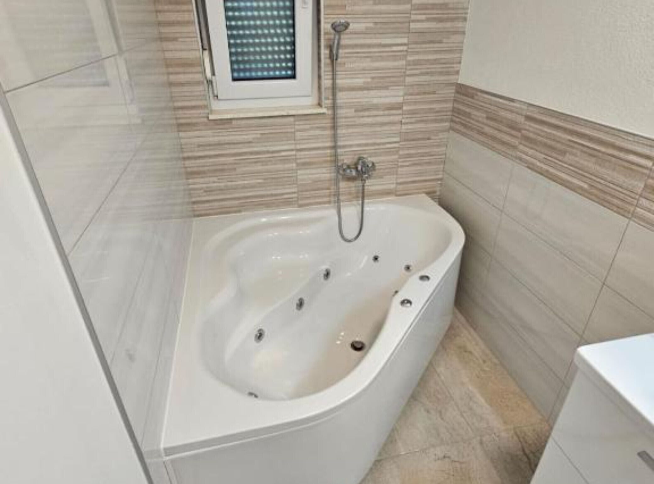 Un baño con una bañera independiente, un cabezal de ducha y una ventana sobre la bañera.