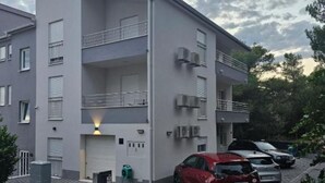 Ein modernes Mehrfamilienhaus mit Garage, ein rotes Auto davor und ein klarer Himmel.