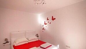A bedroom with a bed, white walls, and a red accent wall with butterfly decorations.