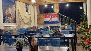 Un espace extérieur aménagé pour les repas, avec des tables et des chaises, un drapeau croate et une vue panoramique sur la côte.