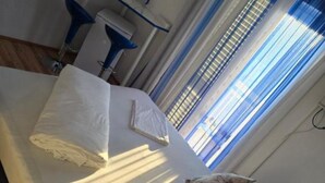 A bed with white linens, a pillow with a floral pattern, and a blue chair in a room with a window and blinds.