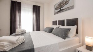 A modern bedroom with a bed, a nightstand, a painting, and curtains.