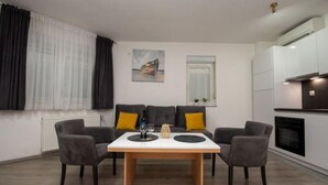 A modern living room with a dining table, grey sofas, and a kitchen area.