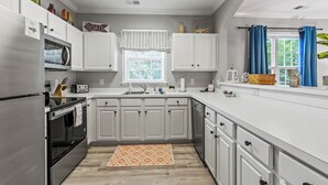 A modern kitchen with white cabinets, a built-in oven, a microwave, and a window with blue curtains.