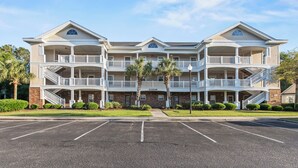 A multi-story hotel with balconies, a parking lot, and a clear sky.