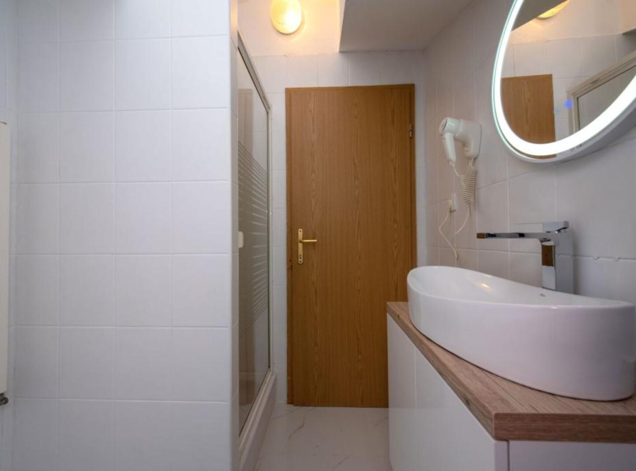 Un baño con puerta de madera, un lavabo blanco y un espejo con luz.