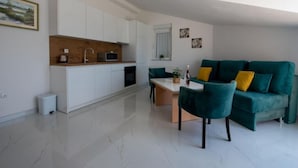 A modern kitchen with white cabinets, a wooden countertop, and a microwave. There is a green sofa with yellow cushions in the living area. - Apartments Tomi - Double Room With Sea View (3) (Trogir)