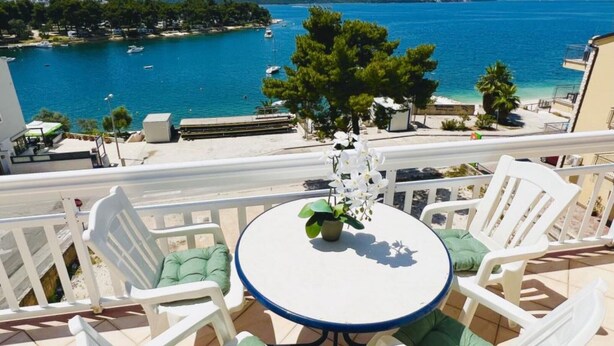 A balcony with a round table and white chairs, overlooking a coastal area with boats and a clear view of the sea. - Apartments Tomi - Classic Double Room With Sea View (9) (Trogir)