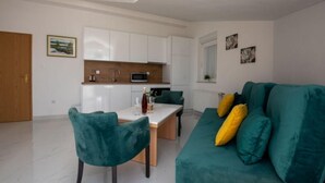 A compact living space with a kitchenette, a dining area, and a sofa with cushions. - Apartments Tomi - Classic Double Room With Sea View (9) (Trogir)