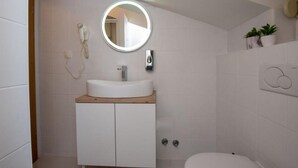 A modern bathroom with a round mirror, a white sink, and a toilet. - Apartments Tomi - Classic Double Room With Sea View (9) (Trogir)