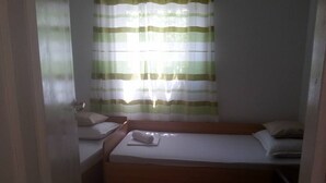 A small, single-bed room with a wooden bed frame, a window with green and white striped curtains, and a white wall. - Apartments Štrbić - One Bedroom - Karlo (Karin Gornji)