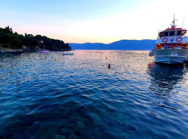 A boat docked at a calm harbor with clear water and distant mountains.