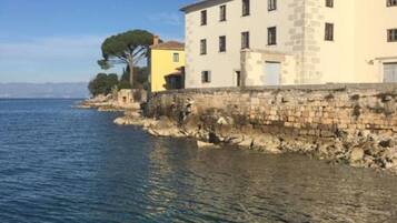 Un edificio costiero con facciata in pietra, un edificio giallo adiacente e vista libera sul mare.