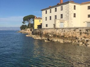 A coastal building with a stone facade, a yellow building adjacent to it, and a clear view of the sea.