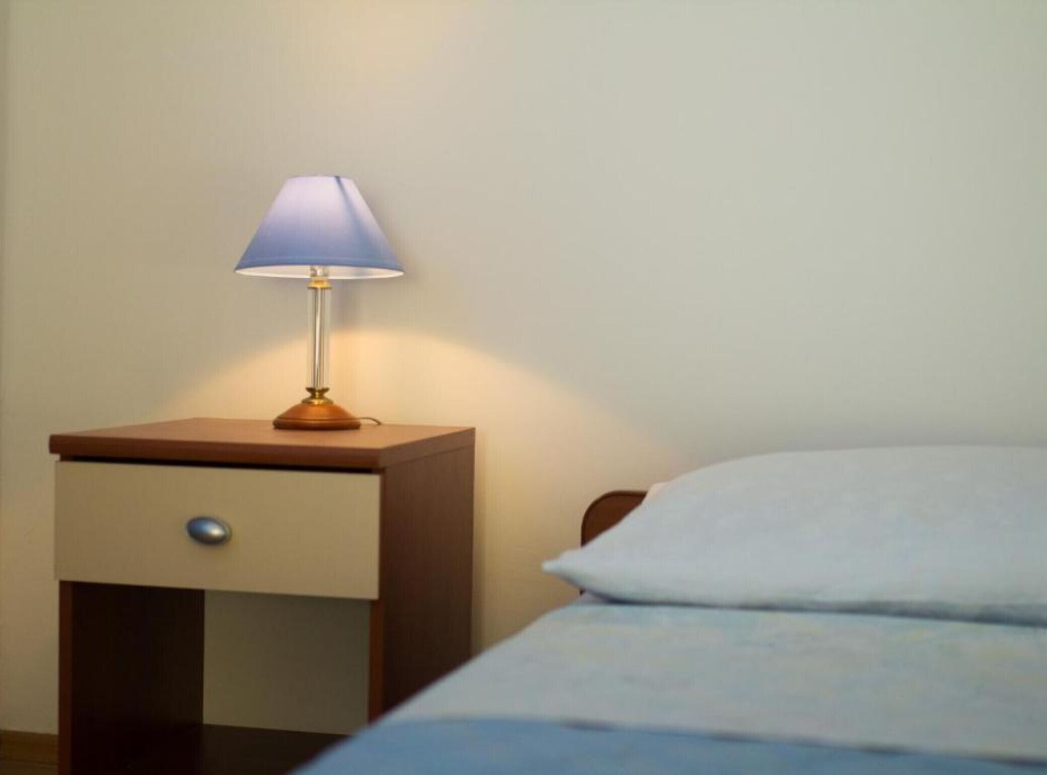 Uma cama com travesseiro branco e mesa de cabeceira com abajur.