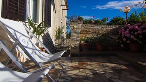 A courtyard with a tiled floor, a white chair, a stone wall, and potted plants.