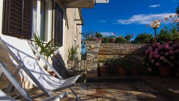 A courtyard with a tiled floor, a white chair, a stone wall, and potted plants.