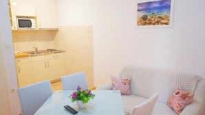 Un espace de vie compact comprenant un coin cuisine, un espace repas avec une table et des chaises, et un canapé agrémenté de coussins décoratifs.