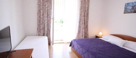 A bedroom with a bed, a desk, and a chair. There is a window with curtains and a painting on the wall.
