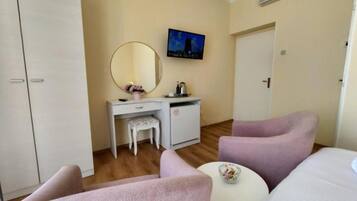 A hotel room with a bed, a desk with a chair, a small table, a mirror, and a television on the wall.