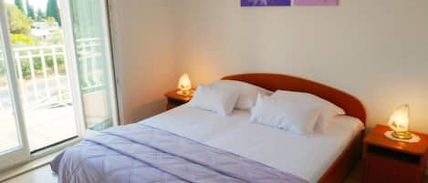 Un dormitorio con una cama, dos mesitas de noche con lámparas, una ventana con vistas a la vegetación y una pared decorada con una pintura floral.