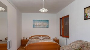 Un dormitorio con una cama de madera, una mesita de noche, una silla, un cuadro y una ventana con marco de madera.