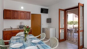 Un comedor con una mesa lista para cuatro personas, armarios de madera, microondas, un refrigerador pequeño y un televisor en la pared.