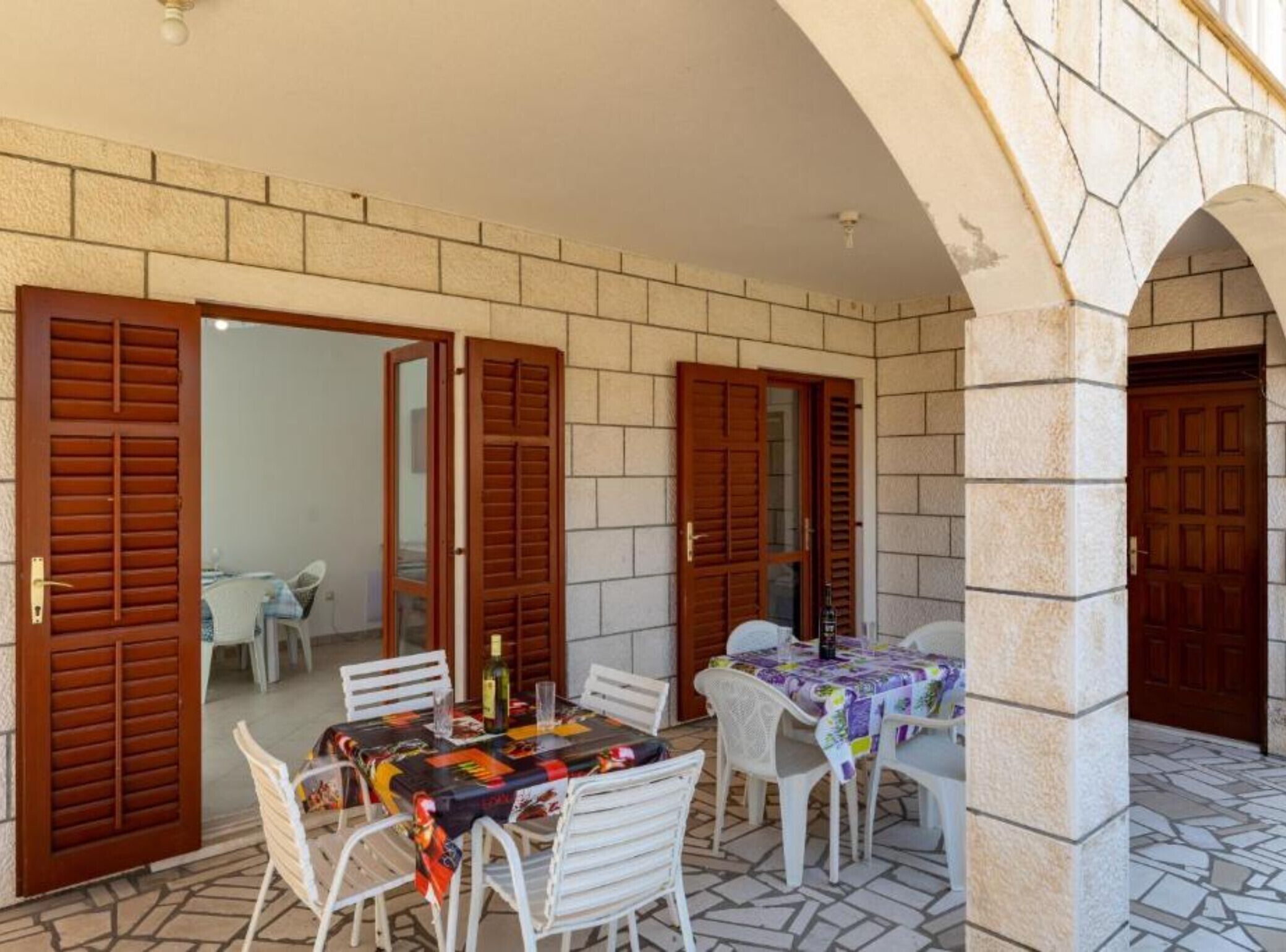Une terrasse extérieure avec une table et des chaises, une bouteille de vin, et une vue sur l’intérieur à travers des portes ouvertes.