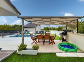 A covered patio with a pool, outdoor furniture, and a barbecue area.