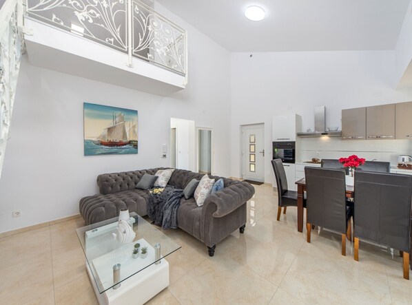 A modern living room with a grey sofa, a glass coffee table, and a dining area with a white table and chairs.