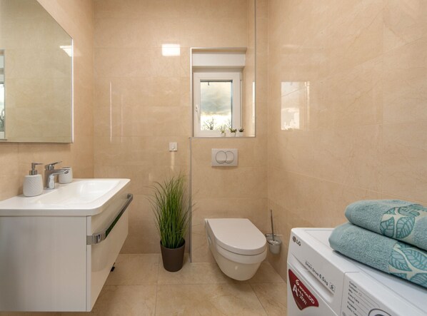 Un baño moderno con lavamanos, inodoro y ventana sobre el inodoro.