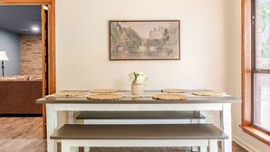 A dining table with woven placemats, a vase with flowers, and a framed landscape painting on the wall.