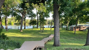 A wooden deck leading to a grassy area with trees and a lake in the background.