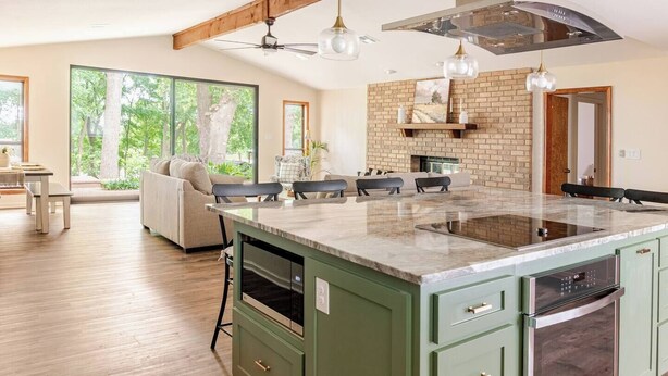 A spacious kitchen with a large island, green cabinetry, and a brick accent wall.