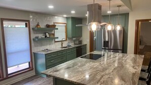 A modern kitchen with a marble island, green cabinetry, and stainless steel appliances.