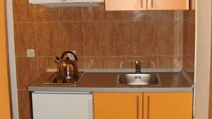Una cocina compacta con armarios naranjas, un refrigerador blanco y una tetera sobre la encimera.
