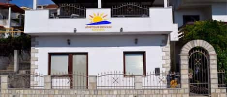 A two-story building with a sign reading "APARTMANI KRIVAC" and a sun symbol.