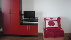 Een kamer met een rode garderobe, een televisie op een zwarte standaard en een bed met een sierkussen in de vorm van een rode roos.