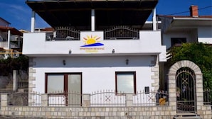Een gebouw met twee verdiepingen, met een bord waarop staat 'APARTMANI KRIVAC' en een zonnesymbool.