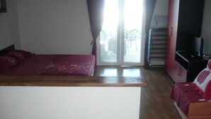 Een slaapkamer met een bed, een slaapbank, een televisie en een schuifdeur naar een balkon.