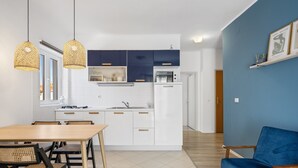 A modern kitchen with white and dark blue cabinets, a dining area with a wooden table and chairs, and a blue sofa in a living space.