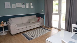 Una sala de estar con un sofá, una mesita redonda y un ventanal con cortinas.