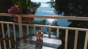 A balcony with a round glass table, a lantern, and a potted plant with pink flowers.