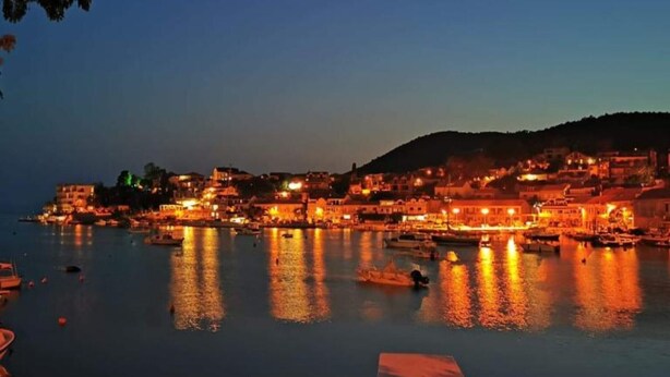 A coastal town at dusk with illuminated buildings and boats on the water.