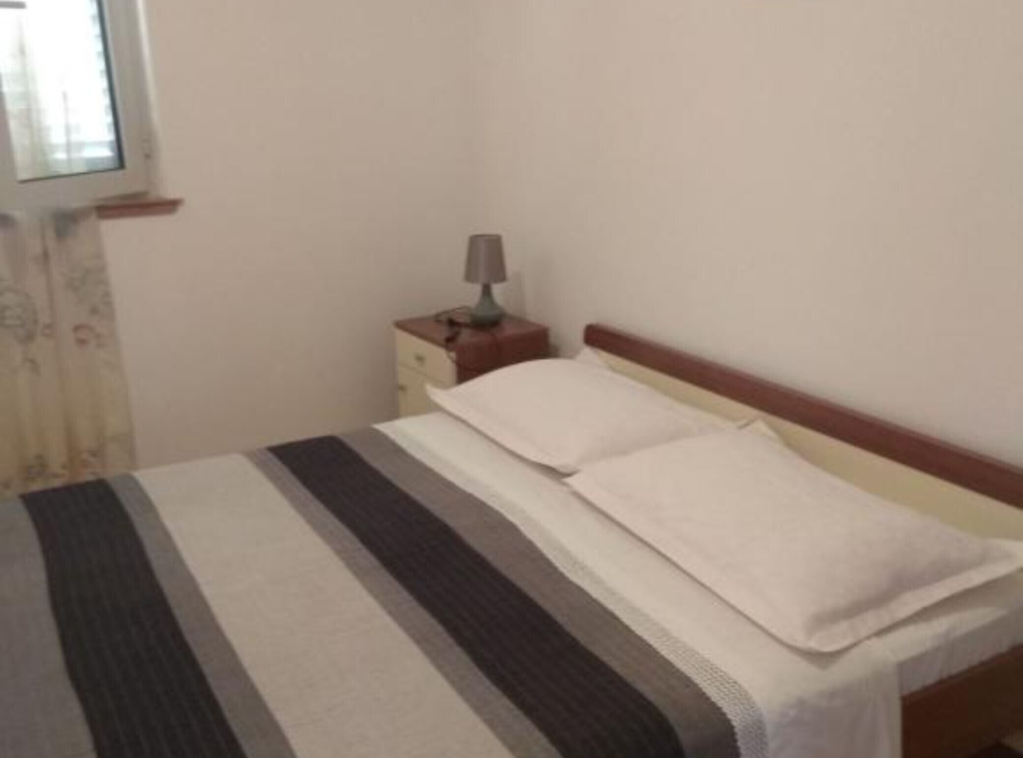 A single bed with a striped bedspread, a bedside table with a lamp, and a window with curtains.